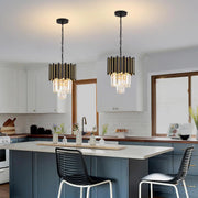 A modern kitchen with blue cabinets and a white island features two Morsale Gio Crystal pendant lights, fitted with LED bulbs and black glass accents, hanging over the island. The room includes white cabinetry, a built-in stove, and large windows for natural light.