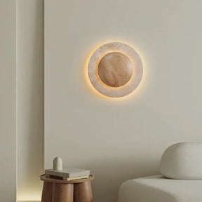 The Natural Travertine LED Decor Wall Light by Morsale.com is a modern LED wall lamp with a circular design, featuring a wooden central circle surrounded by a stone-like ring, both illuminated with a soft, warm glow. Blending Art Deco style and daily lighting needs, this piece creates a serene and ambient atmosphere.