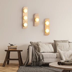 The Natural Travertine Stone LED Wall Lamp by Morsale.com features a modern vertical rectangular base and three evenly spaced, illuminated spherical bulbs that cast a warm, ambient LED light against a neutral background. The base, reminiscent of Art Deco design, is crafted from stone-like travertine with a smooth, curved edge on the left side.