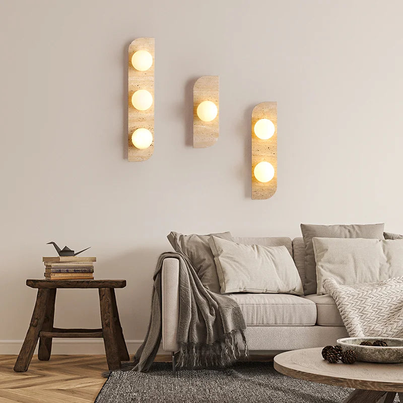 The Natural Travertine Stone LED Wall Lamp by Morsale.com features a modern vertical rectangular base and three evenly spaced, illuminated spherical bulbs that cast a warm, ambient LED light against a neutral background. The base, reminiscent of Art Deco design, is crafted from stone-like travertine with a smooth, curved edge on the left side.