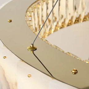 Close-up of an elegant modern ceiling chandelier with a gold circular plate and small gold screws. The fixture hangs by a thin, steel cable and has a reflective surface with intricate, crystal-like components around the edge—perfect for luxury home décor. This is the Natural Marble & Crystal Modern Ceiling Light Fixture from Morsale.com.