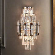 The Morsale Lazzo Crystal Wall Sconce, adorned with cascading crystal prisms and mounted on a neutral-colored wall, perfectly exemplifies contemporary lighting. This LED fixture emits a warm glow that enhances the room's elegance, while its tiered arrangement of crystals beautifully reflects light.