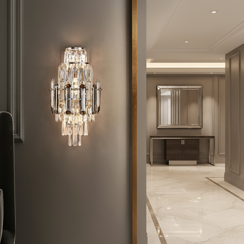 
                  
                    A Morsale Lazzo Crystal Wall Sconce with glass prisms is mounted on a gray wall in an elegant hallway with polished marble floors and a console table beneath a large framed mirror.
                  
                
