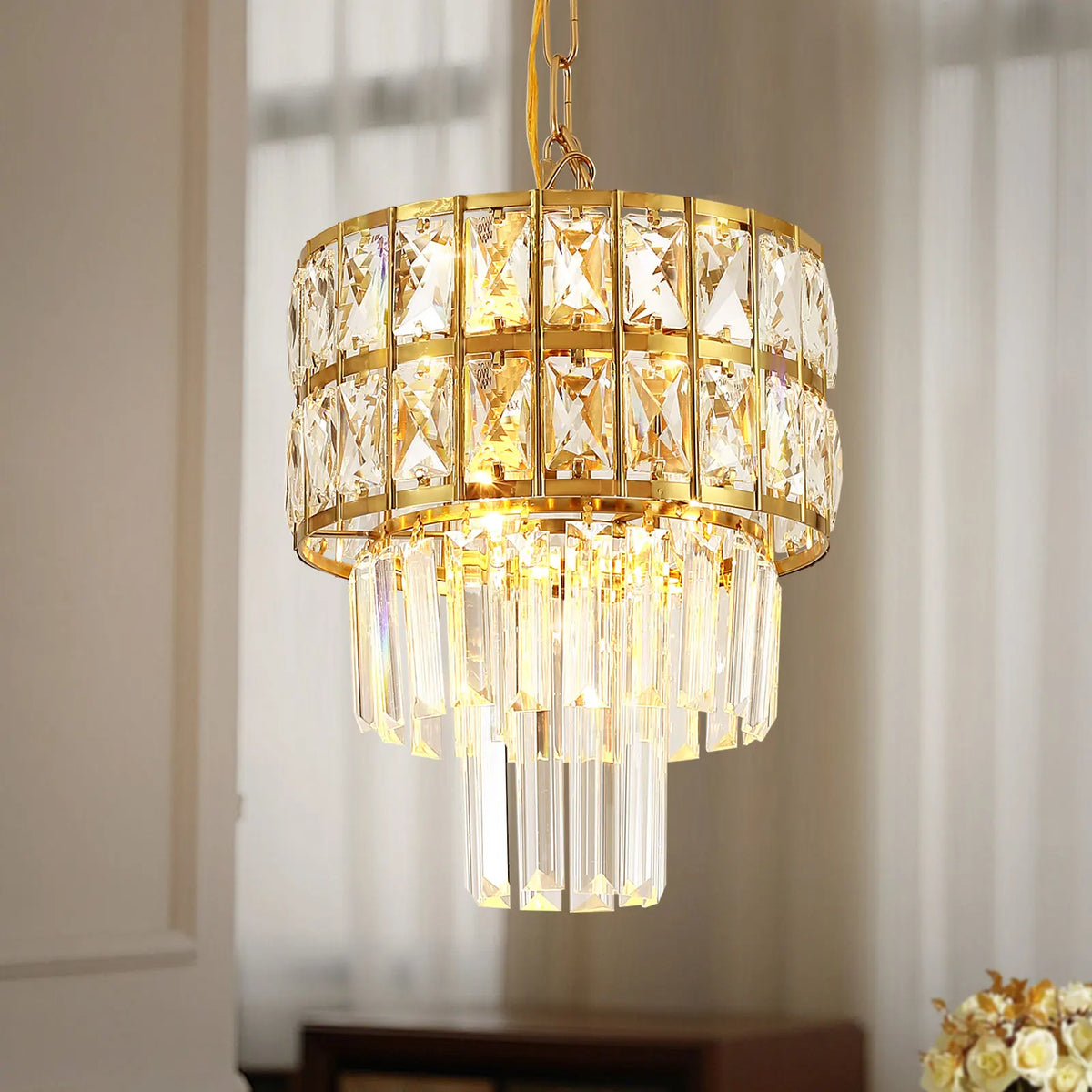 The Gio Crystal Kitchen Pendant Light by Morsale, featuring a gold frame and cascading crystal prisms, illuminates the room with a warm glow. It is elegantly paired with contemporary pendant lights in front of sheer curtains to create a sophisticated ambiance.