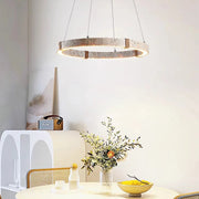 A modern dining space includes a white round table, woven chairs, and the Morsale Natural Travertine Modern Light Fixture with LED bulbs overhead. A glass vase with foliage, a small bottle, and a bowl adorn the table. A white cabinet in the background enhances the contemporary feel.
