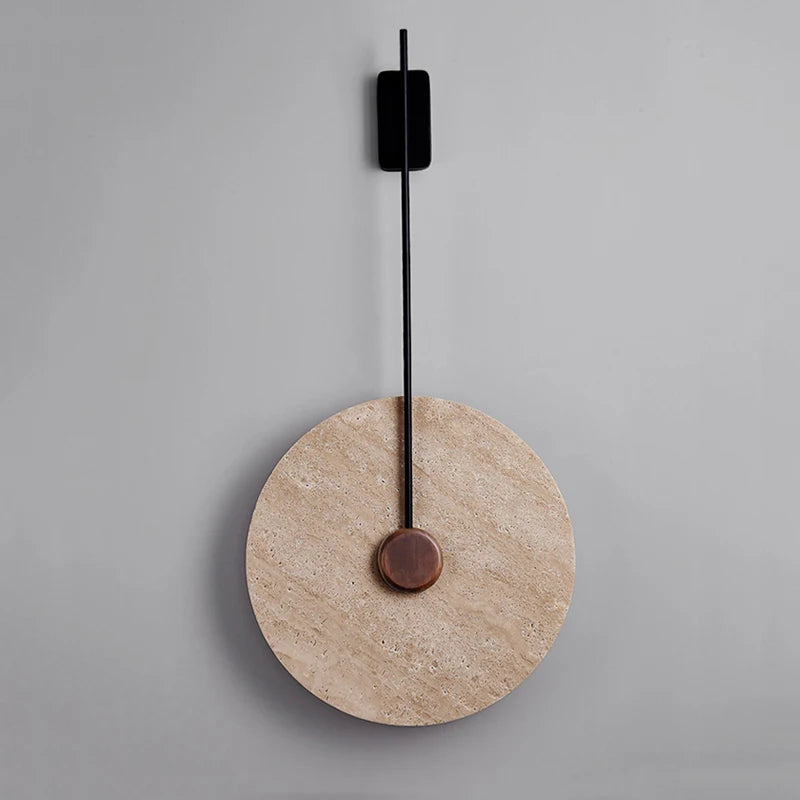 A sleek wall clock featuring a large beige circular face and a slender black pendulum suspended from the top center is mounted on a smooth gray wall, elegantly highlighted by Morsale's Moonshade Natural Marble Sconces, enhancing its minimalist design.