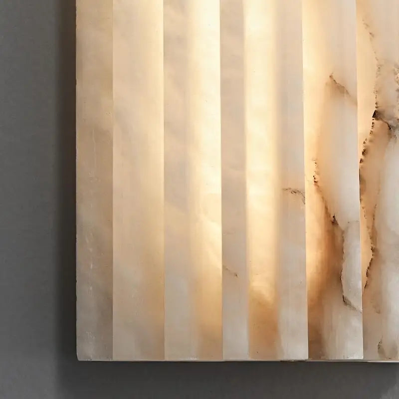 Close-up of Morsale's Natural Marble LED Wall Sconce showcasing translucent vertical ridges and subtle marble-like veining that emit a warm glow, embodying contemporary style against a dark gray background.