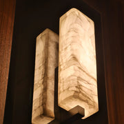 The Alton Marble Wall Lamp by Morsale features two rectangular, marble-patterned light covers that create a warm glow against a dark wooden wall, embodying minimalist aesthetics and adding sophisticated charm to any kitchen space.