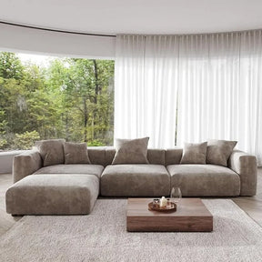 The spacious living room showcases the Corduroy Modern Sectional Couch Sofa by Morsale and a wooden coffee table on a textured rug. Floor-to-ceiling windows reveal a lush green forest, with sheer white curtains partially drawn, enhancing the serene ambiance.