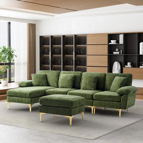 A modern living room showcases a Morsale U-Shaped Sectional Sofa in green velvet with matching ottoman on a gray rug. The sofa, adorned with gold legs, is placed by a large window overlooking greenery, complemented by a wooden shelving unit and decorative items for a chic ambiance.