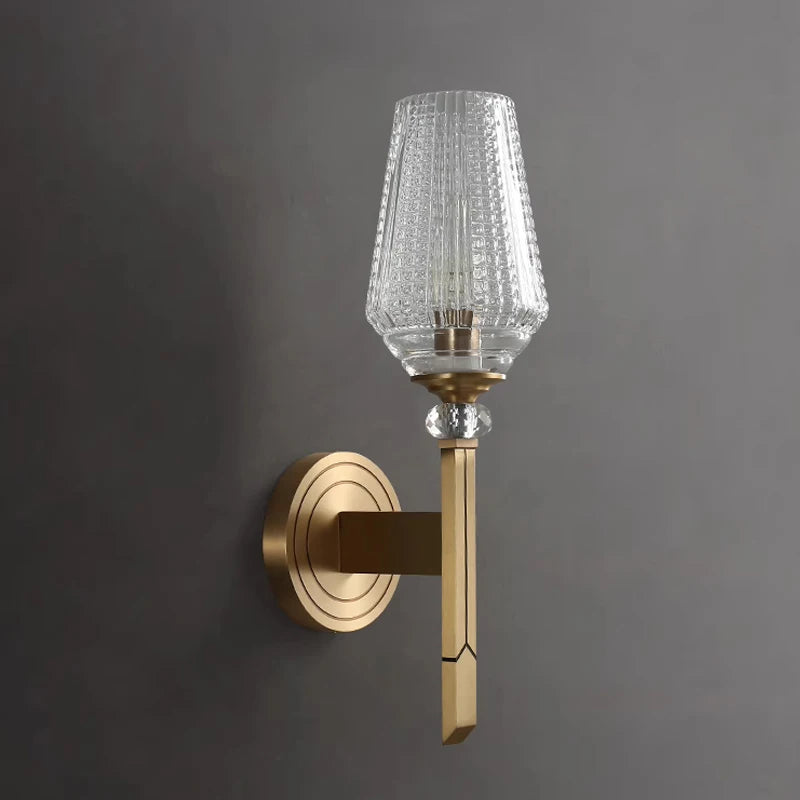 The Palermo Copper & Glass Contemporary Wall Sconce by Morsale features a gold-colored base and a textured glass shade, illuminated with energy-efficient LED light. Crafted from copper, this sconce is mounted on a gray wall, offering a sleek and elegant appearance.