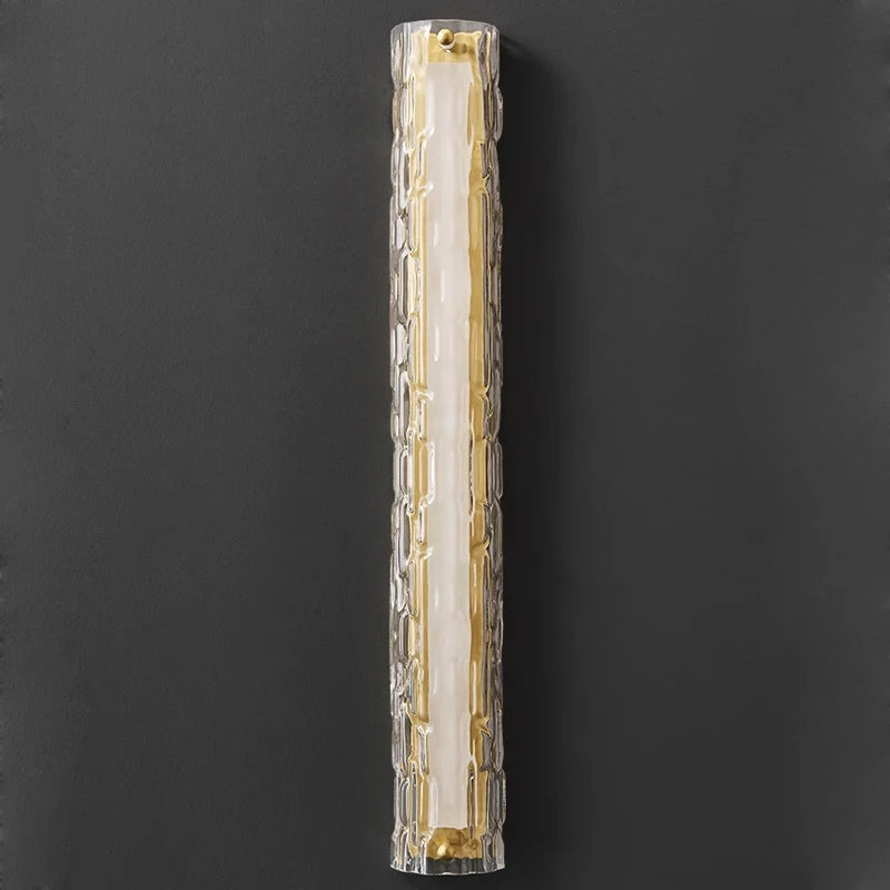 The Postmodern Luxury Glass & Copper Wall Sconce by Morsale features a modern cylindrical design with elongated textured glass, casting a warm golden light that exudes elegance when mounted on a dark wall.