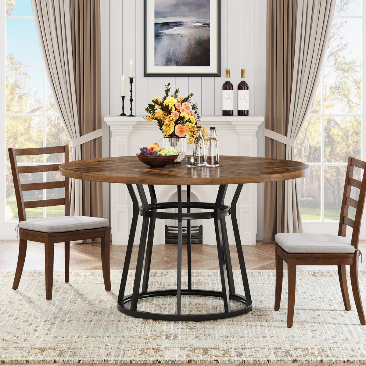 The dining room features a modern style with a Bradford 47-Inch Round Kitchen Dining Table by Morsale and two cushioned chairs. The table holds flowers, a fruit bowl, and water bottles. A fireplace with candles and wine bottles adds warmth, while beige curtains frame the windows elegantly.