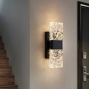 A Water Ripple Crystal Wall Sconce by Morsale illuminates a stairway with wooden steps, next to a textured dark door featuring a metallic handle and keypad lock.