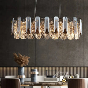 A modern dining room features a large, elegant Lazzo Crystal Ceiling Chandelier by Morsale.com with geometric light fixtures hanging above a marble dining table. The table is set with decorative vases, bowls, and a centerpiece of dried plants. The room has a neutral and sophisticated decor.