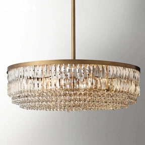 An elegant Bacci Crystal Chandelier from Morsale.com features a luxurious gold finish and cascading tiers of K9 crystals hanging from the ceiling. The crystals are arranged in a layered circular design, reflecting light beautifully. This chandelier exudes a luxurious and sophisticated ambiance.