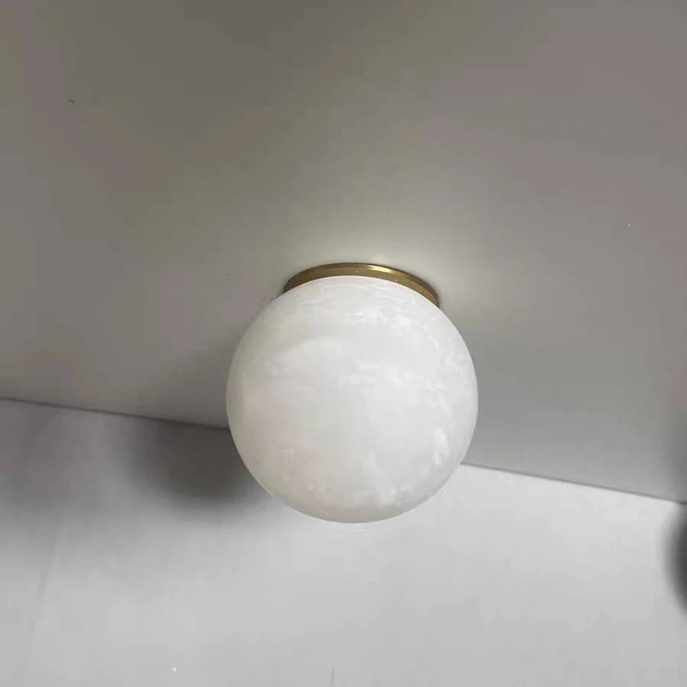 The Moonshade Marble Ball Light Fixture by Morsale, featuring a round frosted glass design and brass base, is mounted on a white ceiling, exemplifying modern style lighting. The light is off, creating subtle shadows.