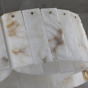 A close-up shot of a Morsale.com 2-Tier Natural Marble Modern Chandelier featuring rectangular, marble-like panels. The panels are white with streaks of beige and brown, and they are connected with small brass fasteners. Copper accents add a touch of elegance to the piece, while the blurred grey background draws focus to its intricate details.