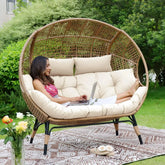 A woman unwinds on the Morsale Winsford Patio Lounge Chair, laptop in hand, surrounded by lush greenery. A patterned rug and flowers adorn the foreground. This modern, cushioned outdoor furniture provides a sunny and serene ambiance ideal for leisurely afternoons.