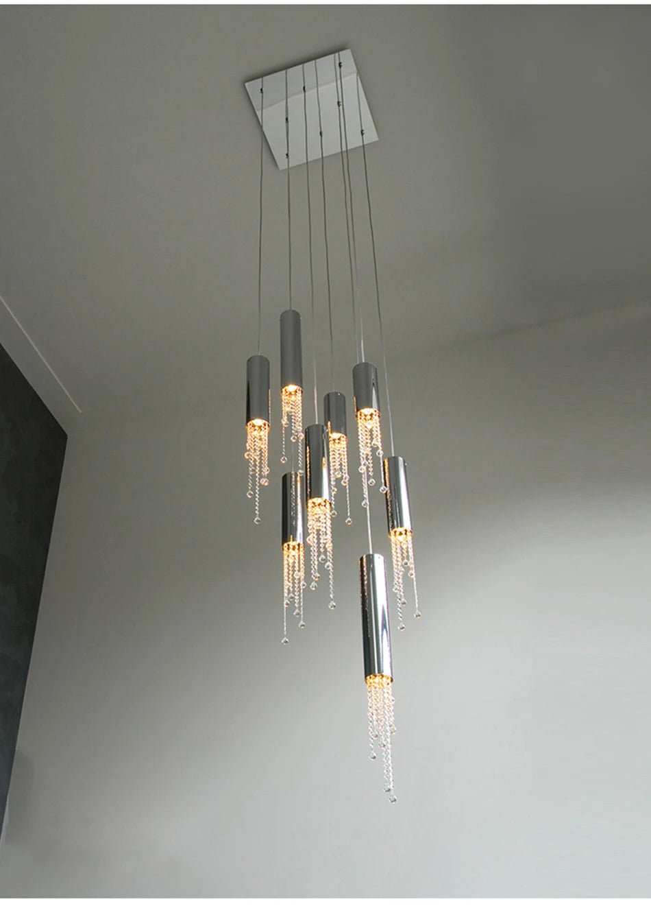 A Canali Modern Crystal Pendant Chandelier from Morsale.com hangs from the ceiling, featuring multiple cylindrical silver lights with warm LEDs. Clear crystals dangle from each cylinder in a cascading fashion, adding an elegant touch to the minimalist interior and enhancing its modern look.