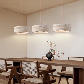 A modern dining area features a wooden table and four chairs with woven backs, illuminated by Morsale's Modern Travertine Pendant Lights. A small black vase with branches and small flowers decorates the table, enhancing the room's minimalist design.