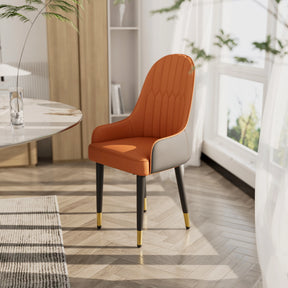 A pair of Morsale's elegant Vegan Leather Dining Chairs, featuring orange leather, black legs, and gold accents, is arranged near a round table in a sunlit room with large windows and a gray patterned rug.