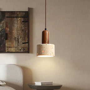 A minimalist kitchen features two Morsale.com Natural Travertine Pendant Lamps with wooden tops and stone-like concrete shades, illuminated by LED bulbs, hanging above a light wood table with a shallow wooden bowl. The background includes a marble backsplash and a counter with minimal décor.