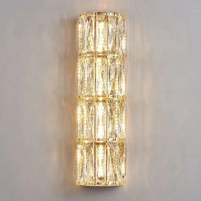 A vertical, cylindrical wall sconce from the Bacci Crystal Wall Lights collection by Morsale.com emits a warm golden light. The fixture features a grid design and is adorned with handmade crystals, creating a sparkling effect against the smooth gray wall.