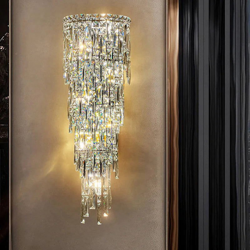 The Bacci Crystal Contemporary Wall Sconce by Morsale emits a warm glow in modern style. This chandelier-style LED wall lamp showcases layered, angular crystal pieces that beautifully reflect light on a neutral-toned wall.