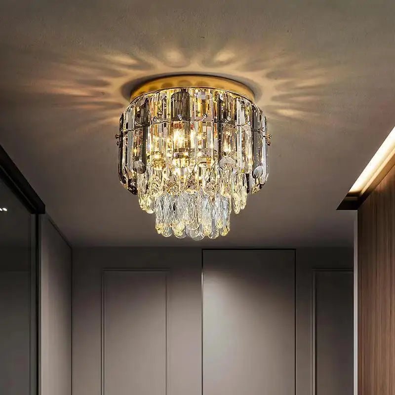 A luxurious crystal chandelier, featuring handmade teardrop-shaped and rectangular crystals, hangs elegantly from a gold ceiling mount. Emitting a warm light that creates sparkling patterns on the ceiling and walls, this Giano Ceiling Light Fixture by Morsale.com adds an elegant touch to the modern room.