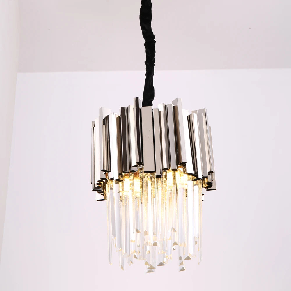 The Gio Crystal Kitchen Light Fixture by Morsale.com hangs from the ceiling, featuring a design of vertical stainless steel rods and suspended K9 Crystal prisms. The crystals catch the light, creating a sparkling effect.