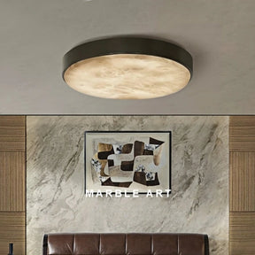 The Moonshade Marble & Copper Ceiling Light by Morsale, featuring a contemporary circular design and energy-efficient LED bulbs, brightens a space adorned with a marble art piece on the wall. A brown leather sofa rests below the artwork, enhanced by wooden panel accents.