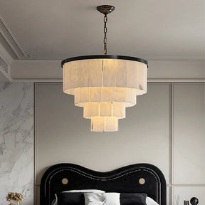 A Morsale Moonshade Marble Chandelier with a black frame and beige translucent panels adorns the modern bedroom ceiling, complemented by a black upholstered headboard, paneled walls, and a striking marble accent wall for an elegant ambiance.