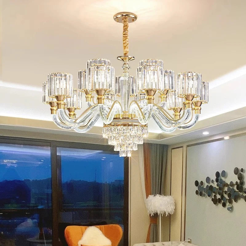 The Morsale Gio Crystal Contemporary Chandelier, featuring luxurious gold accents, hangs elegantly in a modern living room and complements sleek pendant lights. Large windows offer a stunning view of the outdoors, while a cozy armchair and decorative wall art enhance the modern style, all illuminated by energy-efficient LED bulbs.