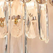A close-up of the Lazzo Crystal Wall Sconce by Morsale showcases a stainless steel frame adorned with multiple elongated smoke grey crystal pendants that reflect light. The crystals are arranged in tiers, casting subtle reflections and enhancing its luxurious appearance.