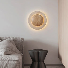 The Natural Travertine LED Decor Wall Light by Morsale.com is a modern LED wall lamp with a circular design, featuring a wooden central circle surrounded by a stone-like ring, both illuminated with a soft, warm glow. Blending Art Deco style and daily lighting needs, this piece creates a serene and ambient atmosphere.