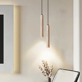 A sleek, cylindrical pendant light from Morsale.com, the Natural Travertine Modern Pendant Light, hangs from the ceiling, casting a warm glow over a small potted plant. The background features a beige wall and a piece of wooden furniture with a light-colored cushion. The scene exudes a minimalist, cozy ambiance.