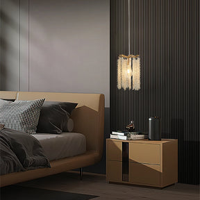 A modern bedroom features a beige bed with striped pillows next to a wooden nightstand holding a book and sleek metal cylinder. Morsale's Albero Crystal Pendant Lights, Set Of 3, hang above, casting a warm glow and enhancing the contemporary ambiance.