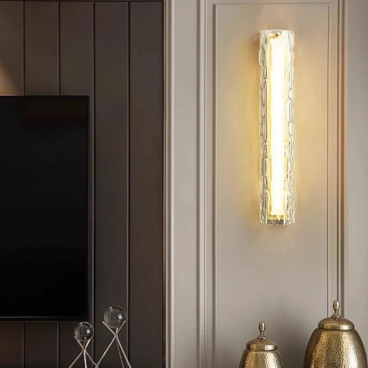 A modern interior showcases the Morsale Postmodern Luxury Glass & Copper Wall Sconces, casting a warm glow on cream paneling. Decorative metallic vases accentuate the surface below, adjacent to a dark-colored wall and offering a glimpse of a flat-screen TV, seamlessly blending elegance with contemporary style.