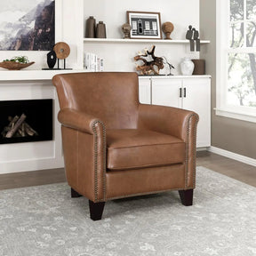 Morsale's Top Grain Genuine Leather Accent Chair is centered on a patterned gray rug. Behind the chair are white cabinets adorned with decorative items, including books and sculptures. A window to the right lets in natural light, while a fireplace sits to the left.