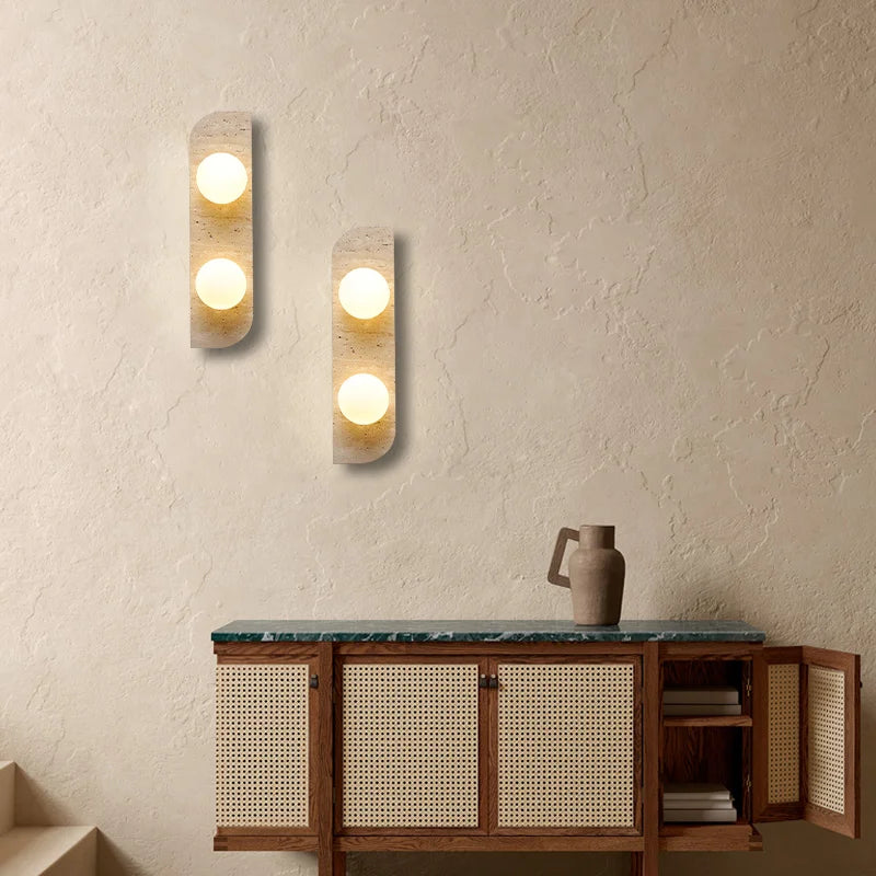 The Natural Travertine Stone LED Wall Lamp by Morsale.com features a modern vertical rectangular base and three evenly spaced, illuminated spherical bulbs that cast a warm, ambient LED light against a neutral background. The base, reminiscent of Art Deco design, is crafted from stone-like travertine with a smooth, curved edge on the left side.