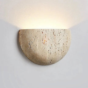 The Contemporary LED Travertine Wall Lamp from Morsale.com, featuring a half-circle design and rustic, textured surface, is mounted on a light-colored wall. This stylish fixture emits a soft, warm light upwards and slightly to the sides, creating a cozy ambiance while offering energy-efficient lighting.