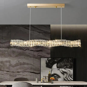 The Bacci Modern Crystal Dining Room Light Fixture by Morsale.com features a sophisticated rectangular pendant design with a gold ceiling mount and two thin wires suspending a crystalline, textured, elongated LED fixture. The light emits a warm glow, enhancing the elegant ambiance against a neutral gray backdrop—an ideal choice for contemporary dining spaces.