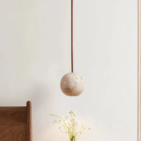 The Travertine Ball Pendant Light Fixture from Morsale.com, crafted from natural travertine stone, features a beige, porous surface that exudes a rustic and organic charm as it hangs from the ceiling. This elegant light fixture is suspended by a brown cord against a plain, off-white background.