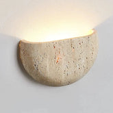 The Contemporary LED Travertine Wall Lamp from Morsale.com, featuring a half-circle design and rustic, textured surface, is mounted on a light-colored wall. This stylish fixture emits a soft, warm light upwards and slightly to the sides, creating a cozy ambiance while offering energy-efficient lighting.