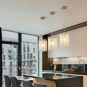 The modern kitchen features three Morsale Alleri Crystal Pendant Lights above a sleek island. Large windows flood the space with natural light, while minimalist cabinetry, chairs, a sleek faucet, and fresh ingredients enhance the contemporary design.