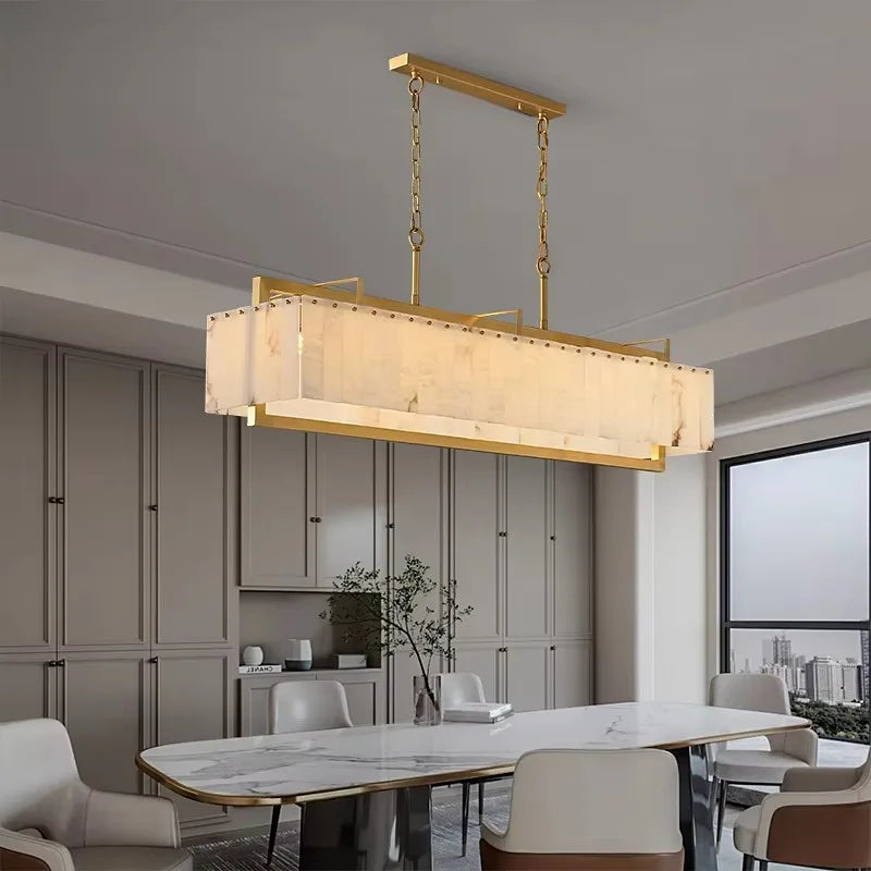 A modern dining room showcases a rectangular marble table with white chairs, illuminated by the Stanton Brass & Marble Dining Room Chandelier by Morsale, featuring LED bulbs and a frosted glass shade suspended by gold chains.