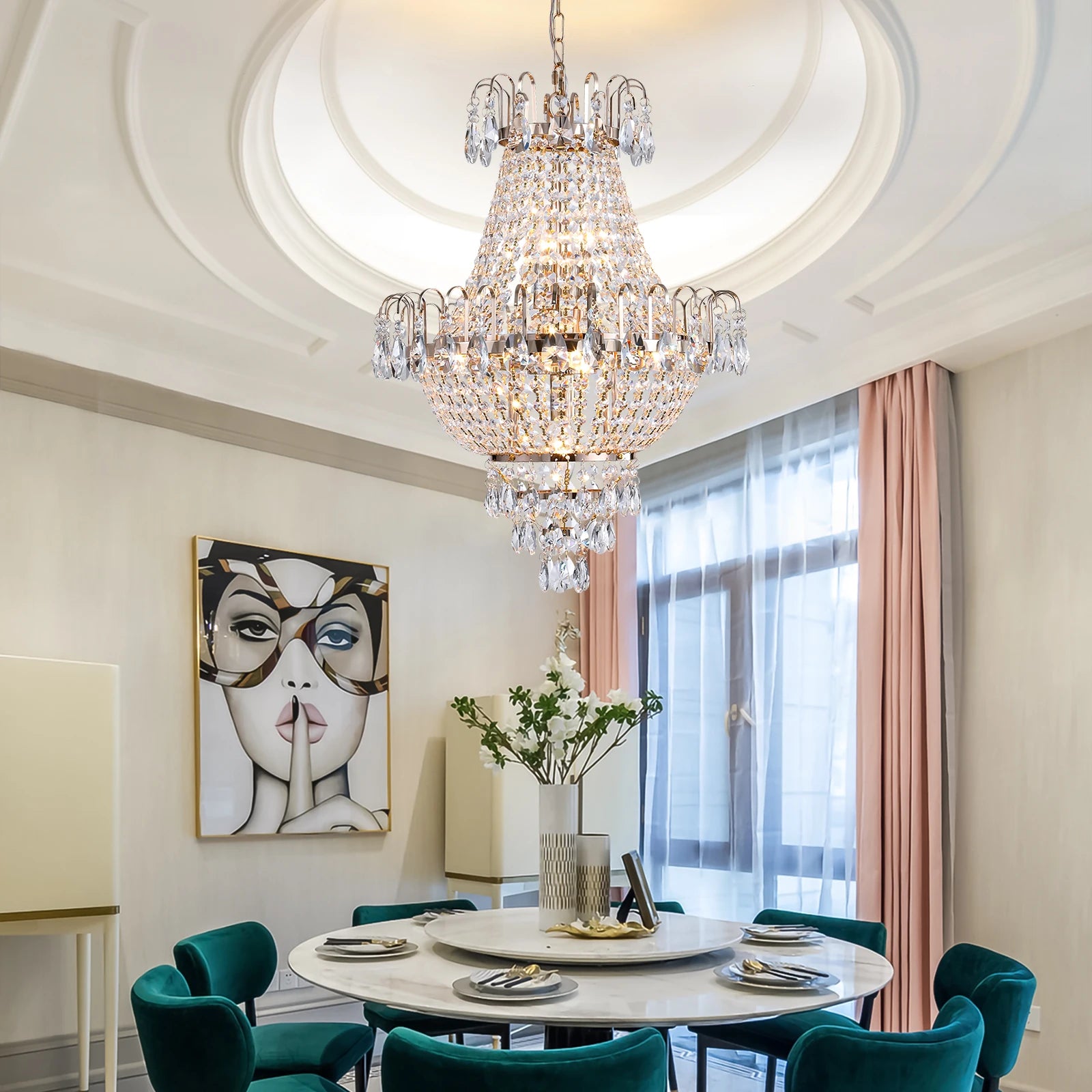 A dining room features a circular table set for five, surrounded by teal velvet chairs. Above, the Morsale French Empire Crystal Chandelier adds elegance with its modern style. Curtains frame a window, and a modern art piece depicting a woman's face adorns the wall.