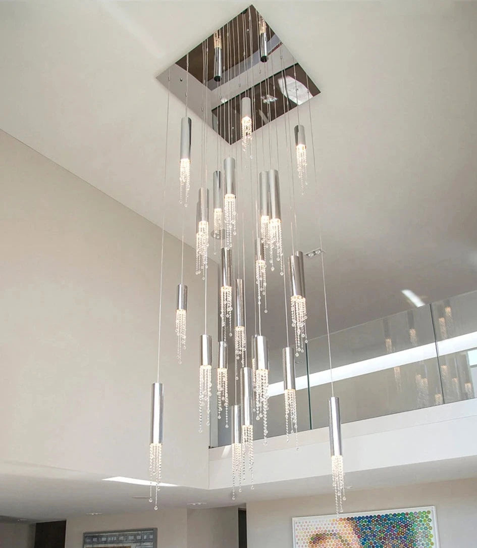A modern living space with a high ceiling features a Canali Modern Crystal Pendant Chandelier by Morsale.com, composed of multiple hanging lights adorned with clear crystals. On the walls are two large, colorful artworks. A glass vase with flowers sits on the dining table below, while a glass railing can be seen on an upper level.
