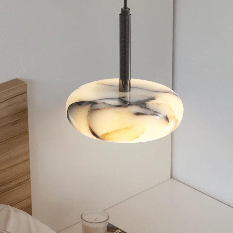 The Natural Marble Pendant Lamp by Morsale, featuring LED bulbs and a cream-black marble shade, illuminates a minimalistic bedroom. A wooden headboard and white surface with a glass candle accentuate the sleek modern style.